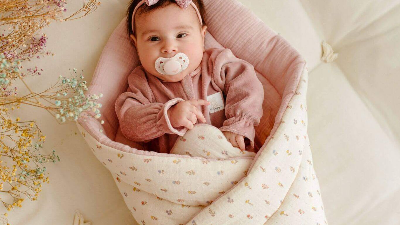 A baby wrapped in a floral swaddle with a pacifier and bow.