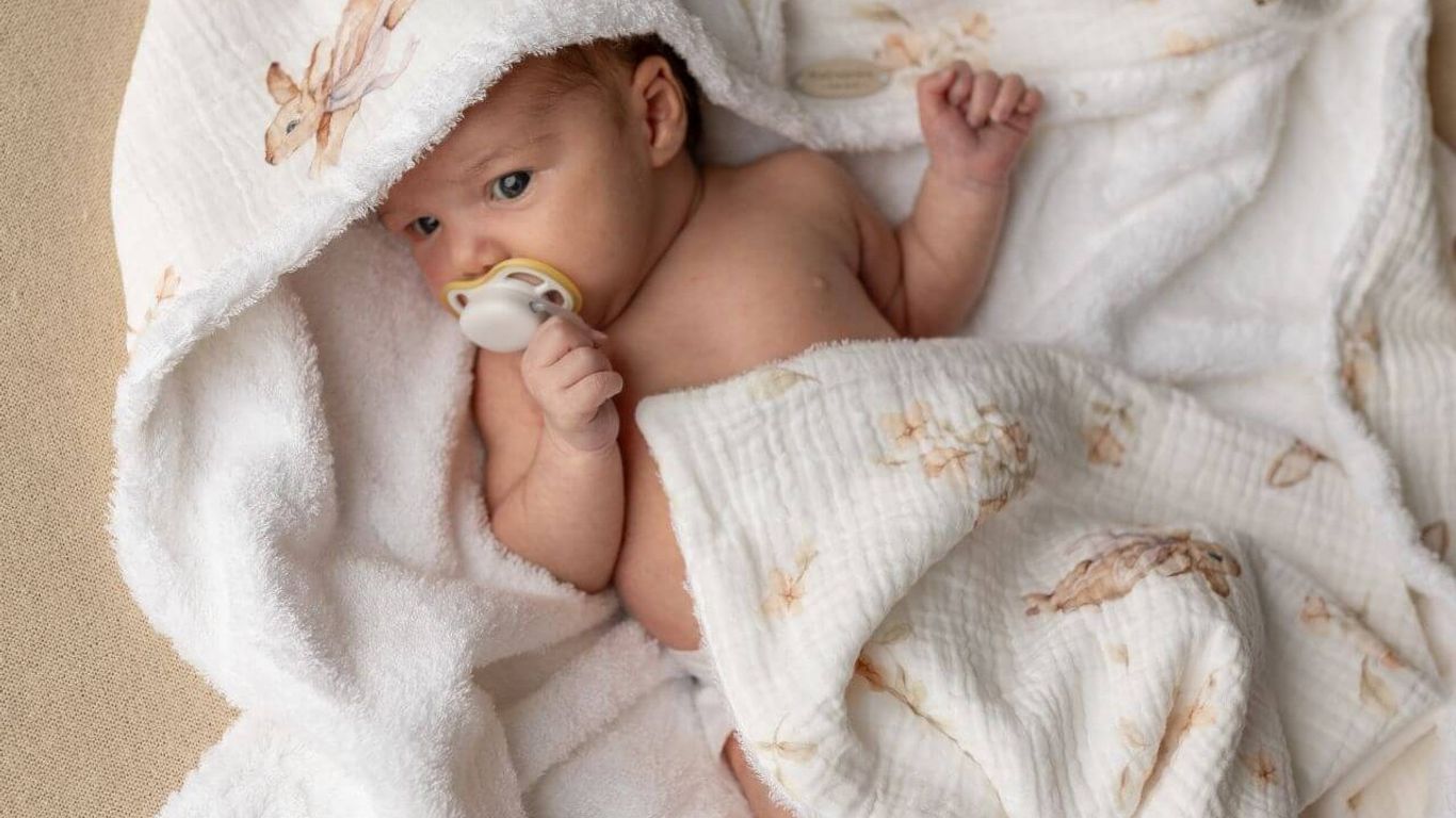 A baby wrapped in a white blanket with bunny prints and a pacifier.