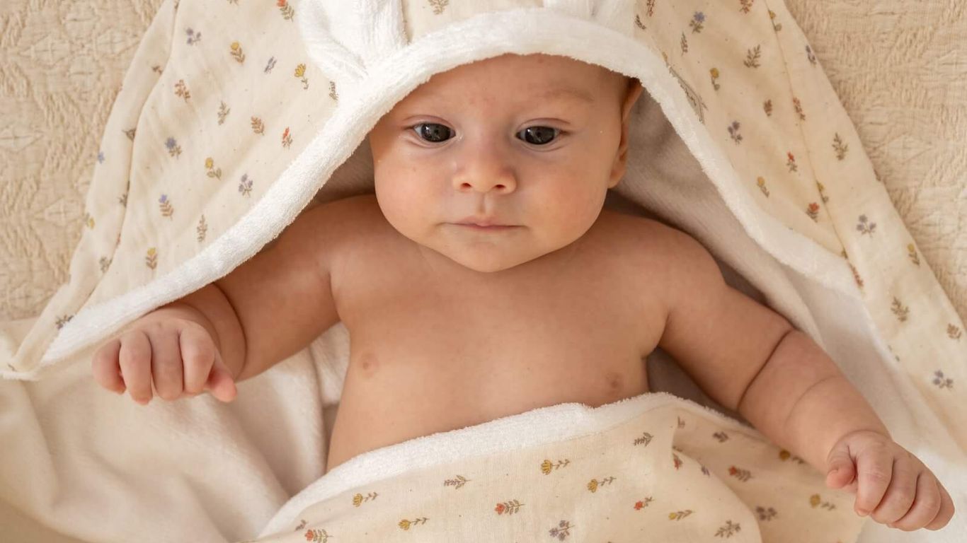 A baby wearing a hooded towel with bunny ears, wrapped in a floral blanket.