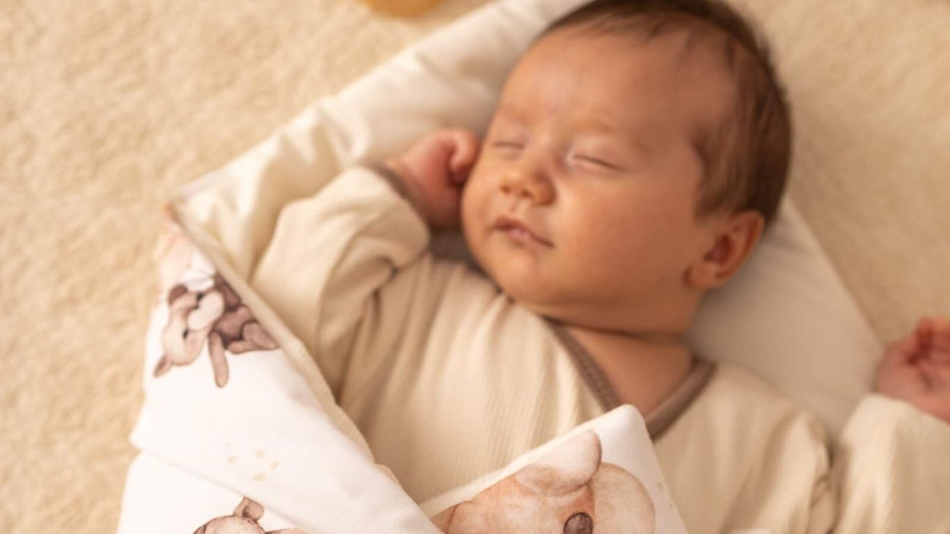 A baby sleeps peacefully wrapped in a teddy bear patterned blanket.