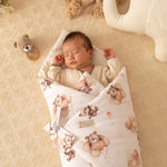 Newborn baby wrapped in a floral blanket with teddy bear patterns on a beige surface.