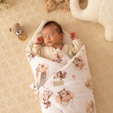 Newborn baby wrapped in a floral blanket with teddy bear patterns on a beige surface.