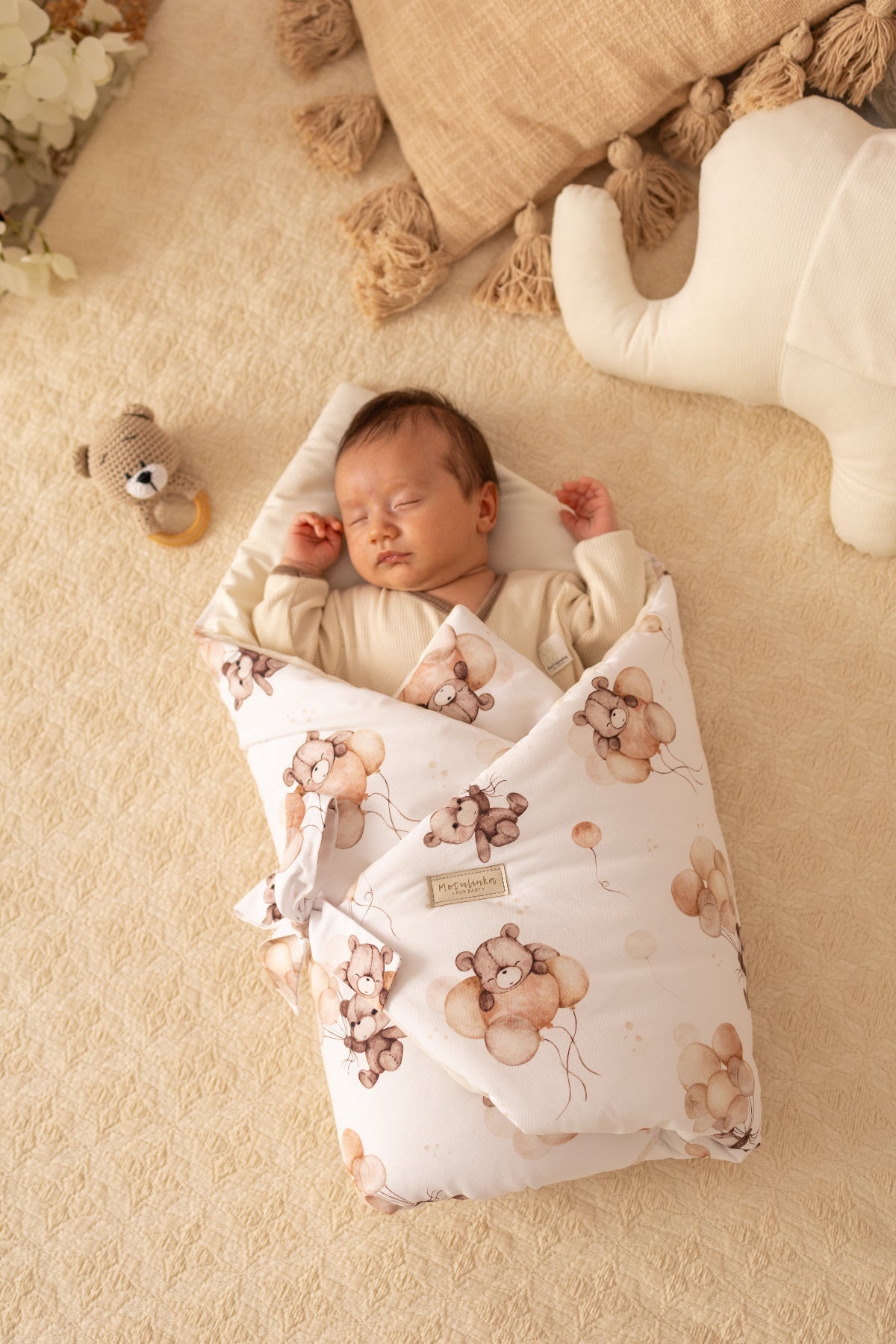 Newborn baby wrapped in a floral blanket with teddy bear patterns on a beige surface.