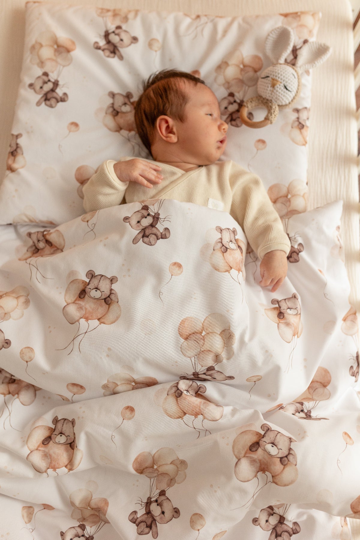 Baby lying on a crib with teddy bear patterned bedding
