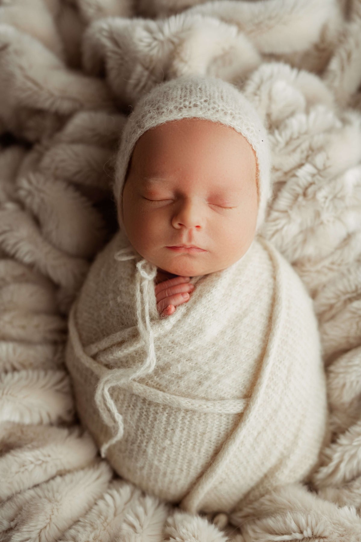 Sleeping newborn swaddled in a cream knit wrap and bonnet