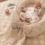 Newborn baby in a textured beige crib with soft toys in the background