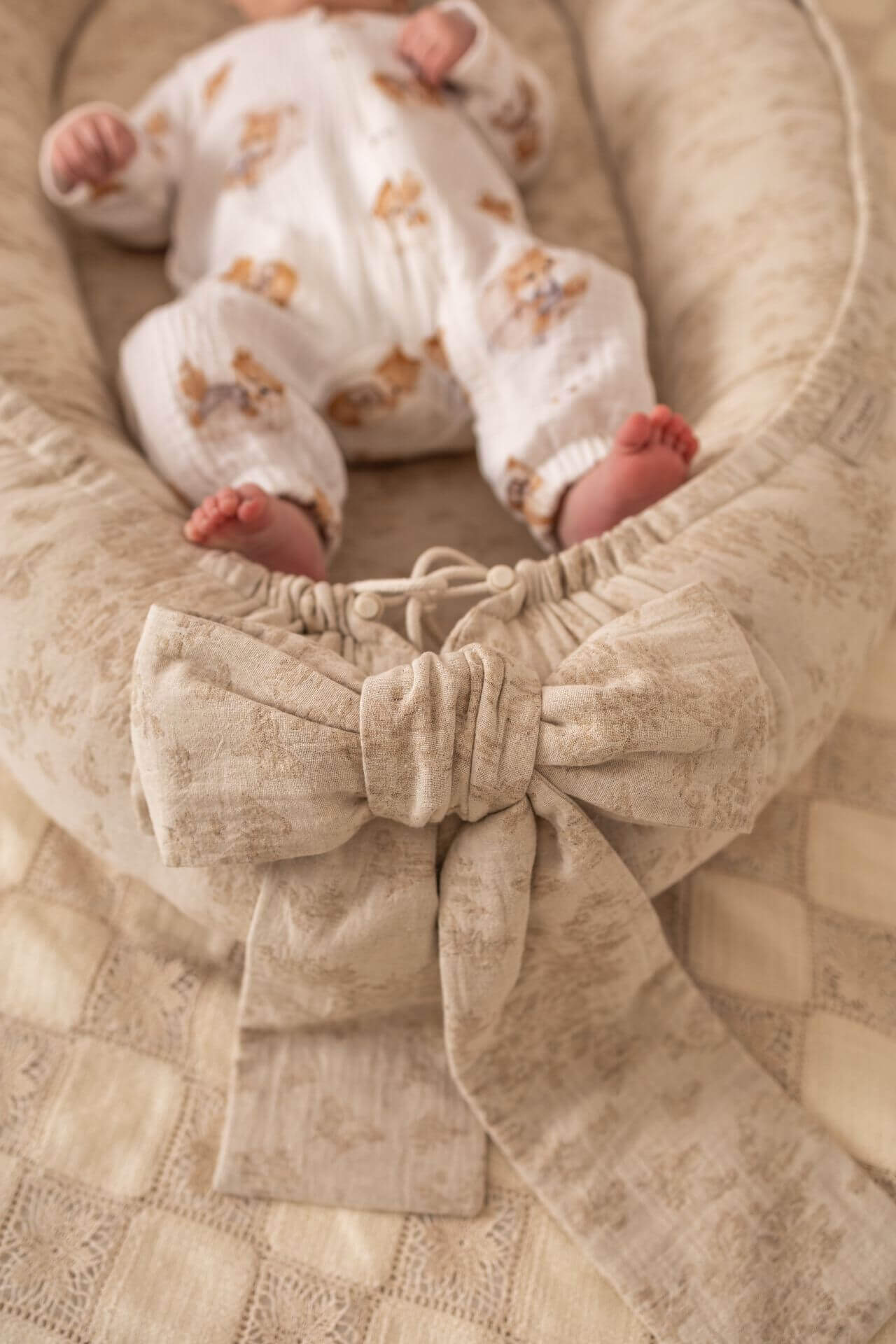 Baby in a white onesie with floral patterns lying in a textured beige crib.
