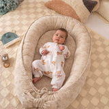 Baby in a cozy beige crib with soft pillows and toys in a warm, homey setting.