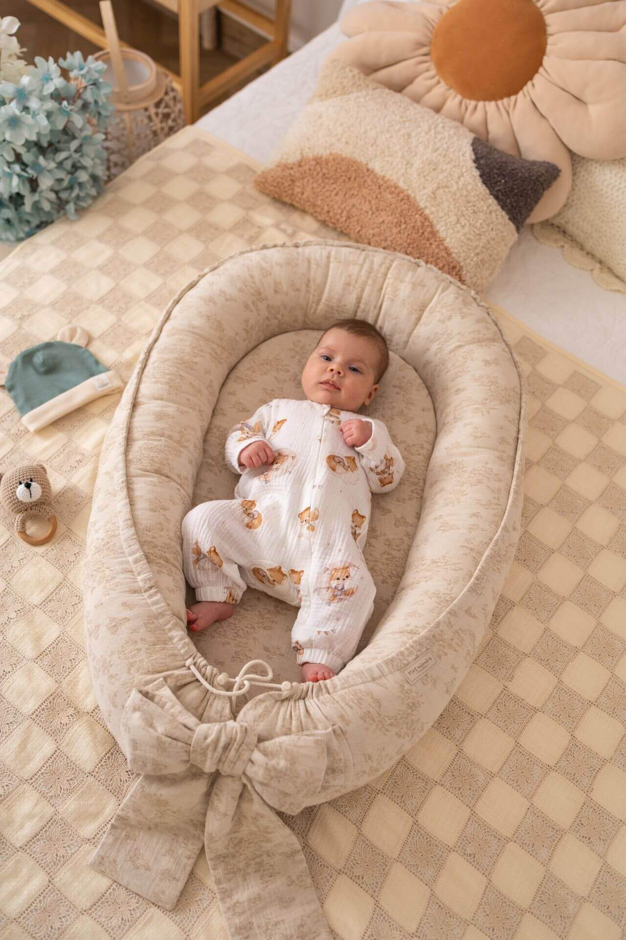 Baby in a cozy beige crib with soft pillows and toys in a warm, homey setting.