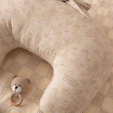 Beige baby pillow with a bow and a small toy on a checkered floor