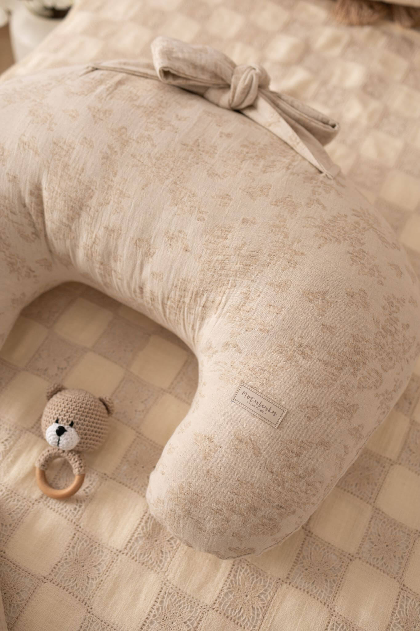 Beige baby pillow with a bow and a small toy on a checkered floor